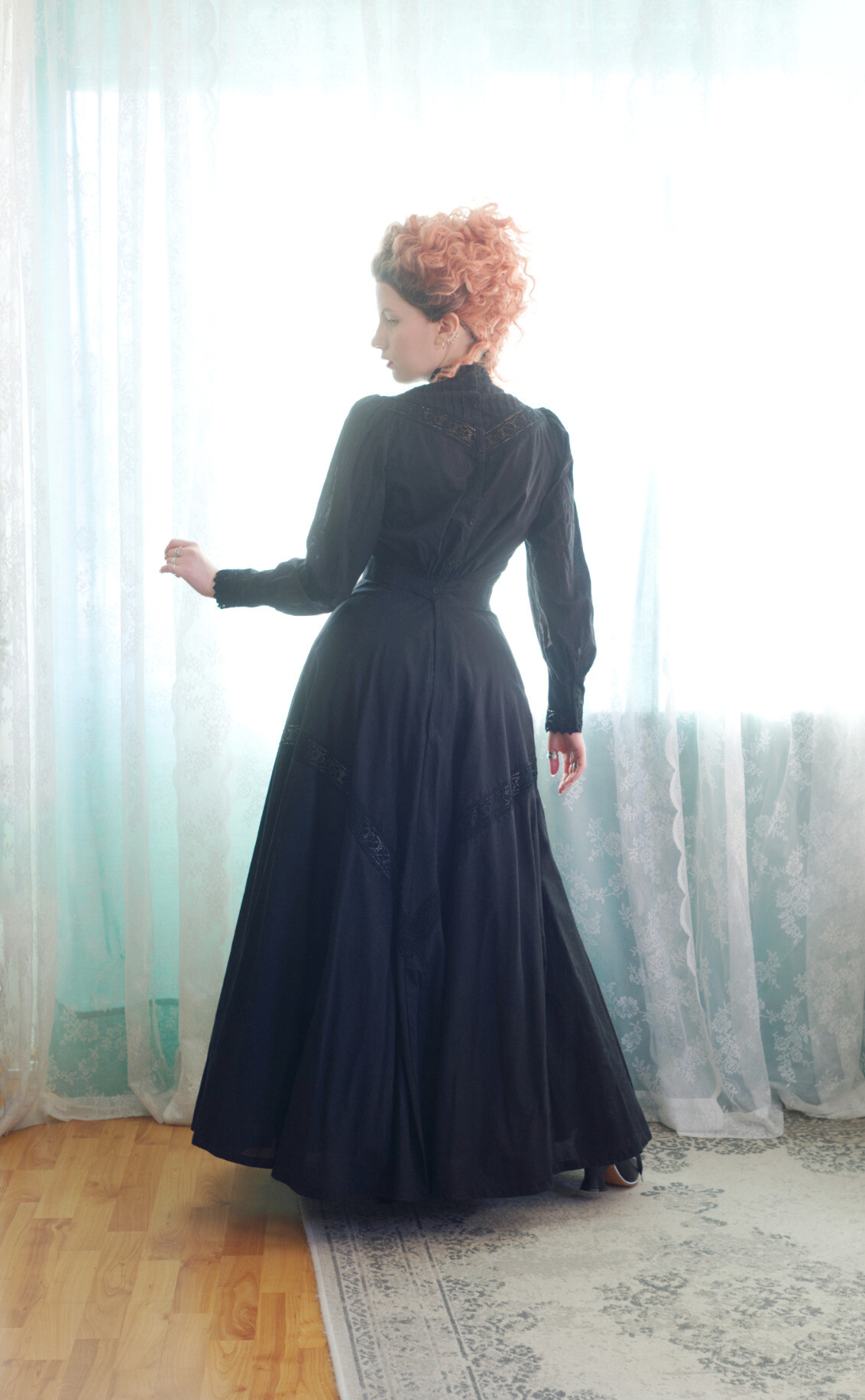 A photo of the same from the back. Her hair is swept aside, unlike in the second photo in the thread. Here you can see the delicately puffed sleeves, the back fullness gathering to the waist at the centre back and the row of buttons. There is a lace insertion and pin tuck detail at the back yoke and the high collar doesn't have buttons, but rather snaps. You can just see the heels of her shoes peeking from under the back hem.