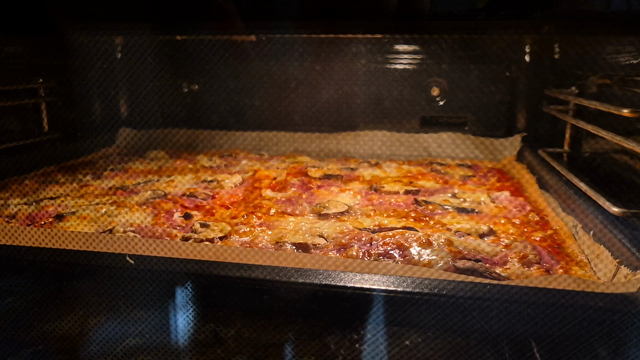 Pizza im Ofen auf einem Blech. Der Teig schlägt in der Hitze Blasen.
