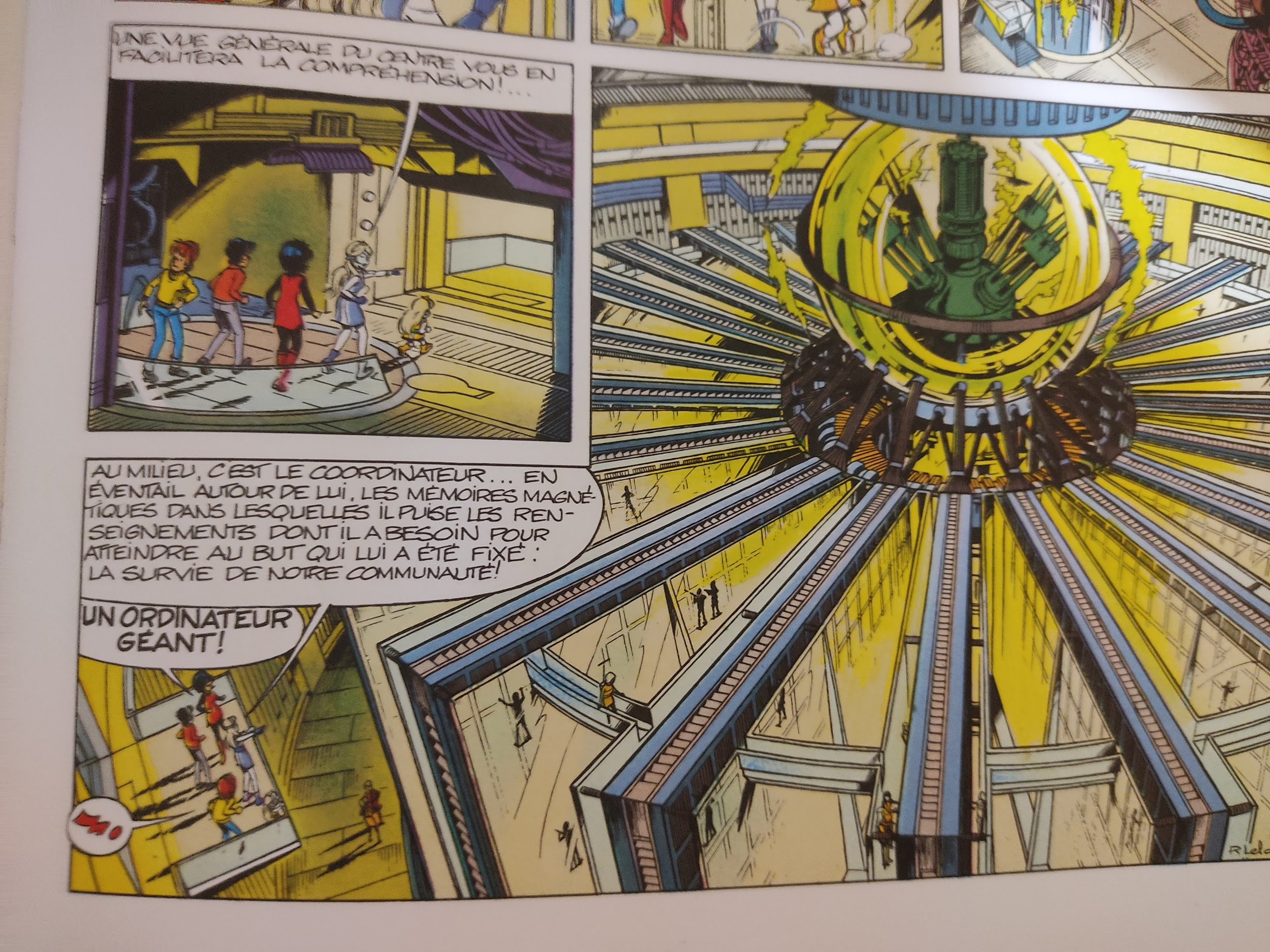 Demi page d'album de BD. On y voit un ordinateur gigantesque enfermé dans une bulle de verre, connecté à d'immenses banques de données. Le tout forme un cylindre d'une cinquantaine de mètres de diamètres, sur une hauteur inconnue puisque le dessin montre que les banques de données s'enfoncent dans les profondeurs. Demi page d'album de BD. On y voit un ordinateur gigantesque enfermé dans une bulle de verre, connecté à d'immenses banques de données. Le tout forme un cylindre d'une cinquantaine de mètres de diamètres, sur une hauteur inconnue puisque le dessin montre que les banques de données s'enfoncent dans les profondeurs.