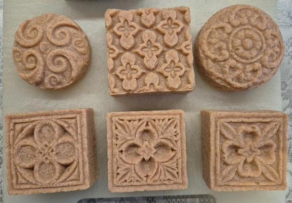 6 Seifen in der Farbe von rotem Sandstein. Zwei runde Stücke, 4 quadratische. Die Muster erinnern an Steinmetzarbeiten an alten Kirchen.