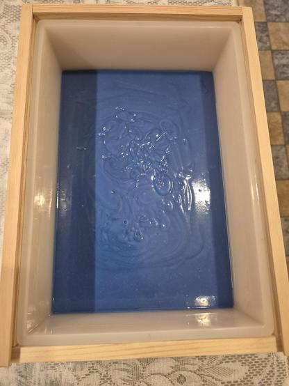 Seifenform aus Silikon in einem Holzkasten, darin eine Schicht blauer Seifenleim.