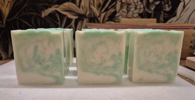 Frisch geschnittene Seifenstücke auf einem weißen Plastikbrett. Die Stücke sind gelblich weiß mit einem verschwommenen grünen Muster und unregelmäßigen, gelben Punkten.