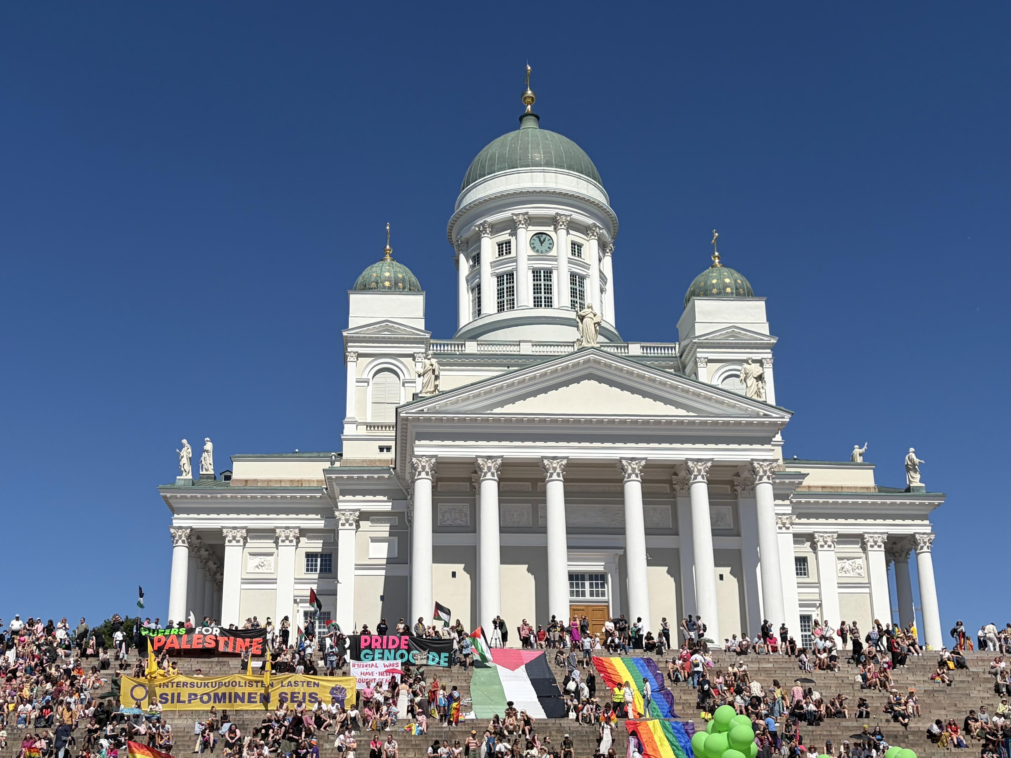 Helsinki Cathedral with “Queers for Palestine” and a large Pride flag on the steps in front of it