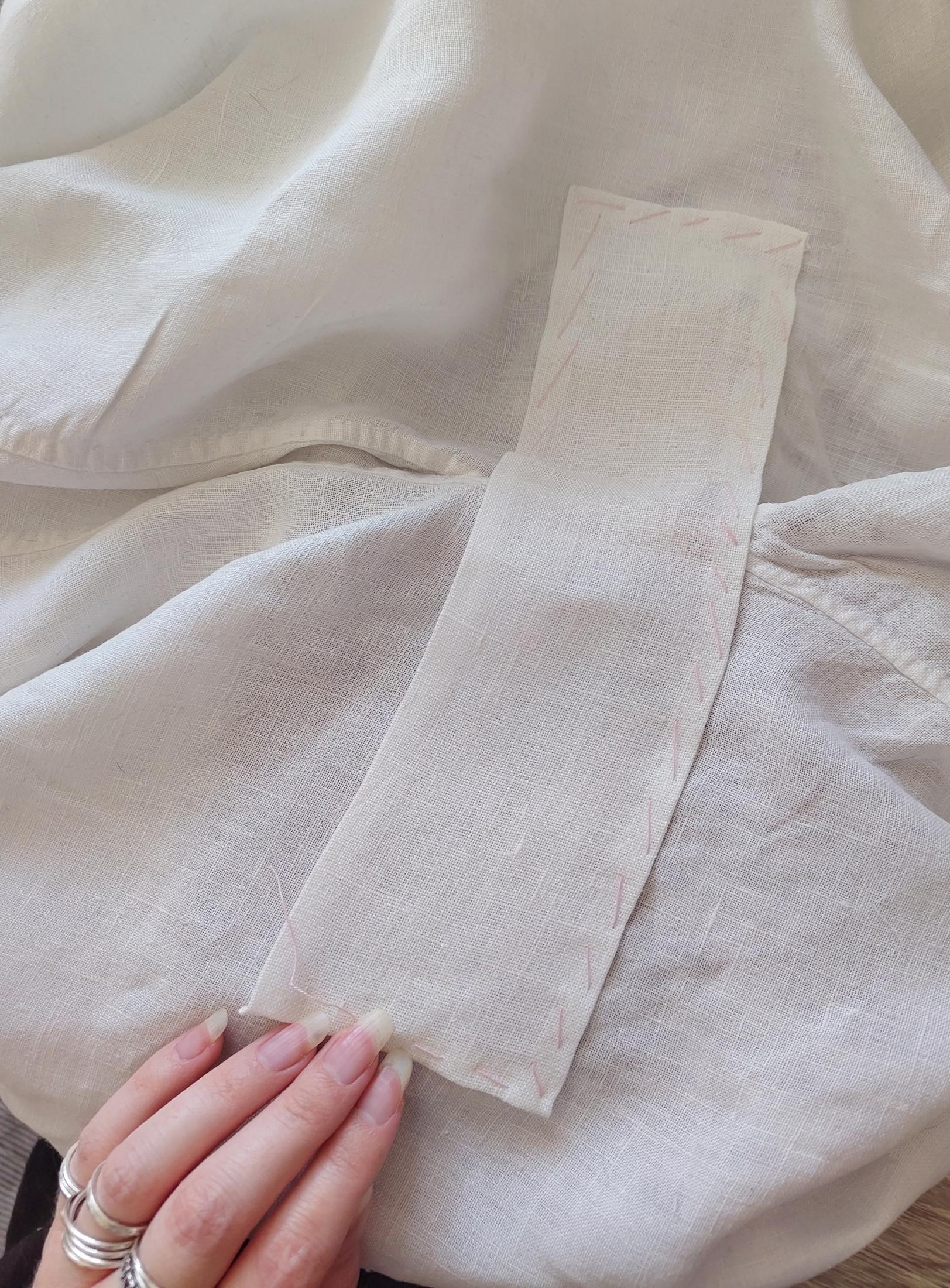 A rectangular patch of different white linen fabric slapped on and tacked into place with loose stitches in pink basting thread. It's not even entirely straight on there, but does fully cover up and join the torn bits, which are now hidden.