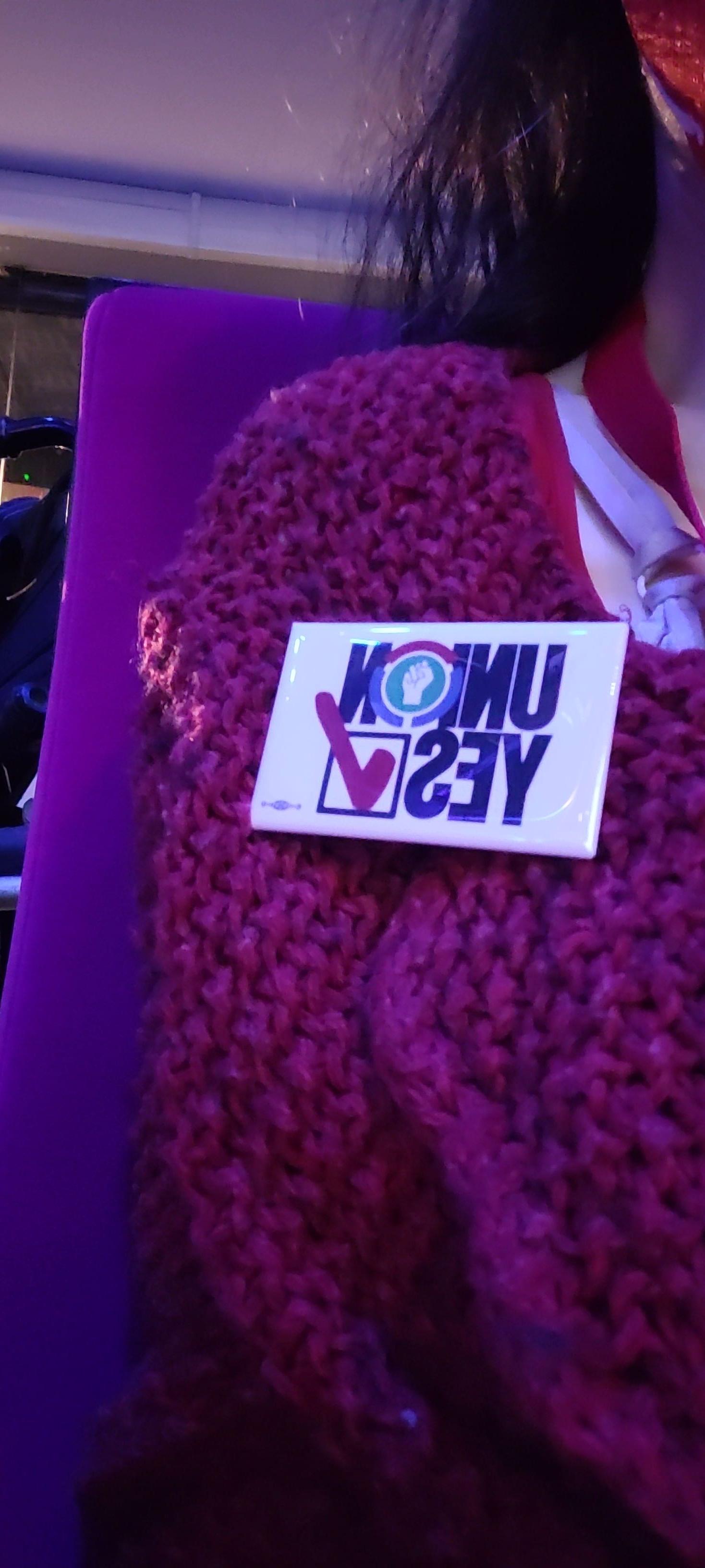 Picture of a knitted red shawl maintained in place with a pin's marked "union yes" with a check mark