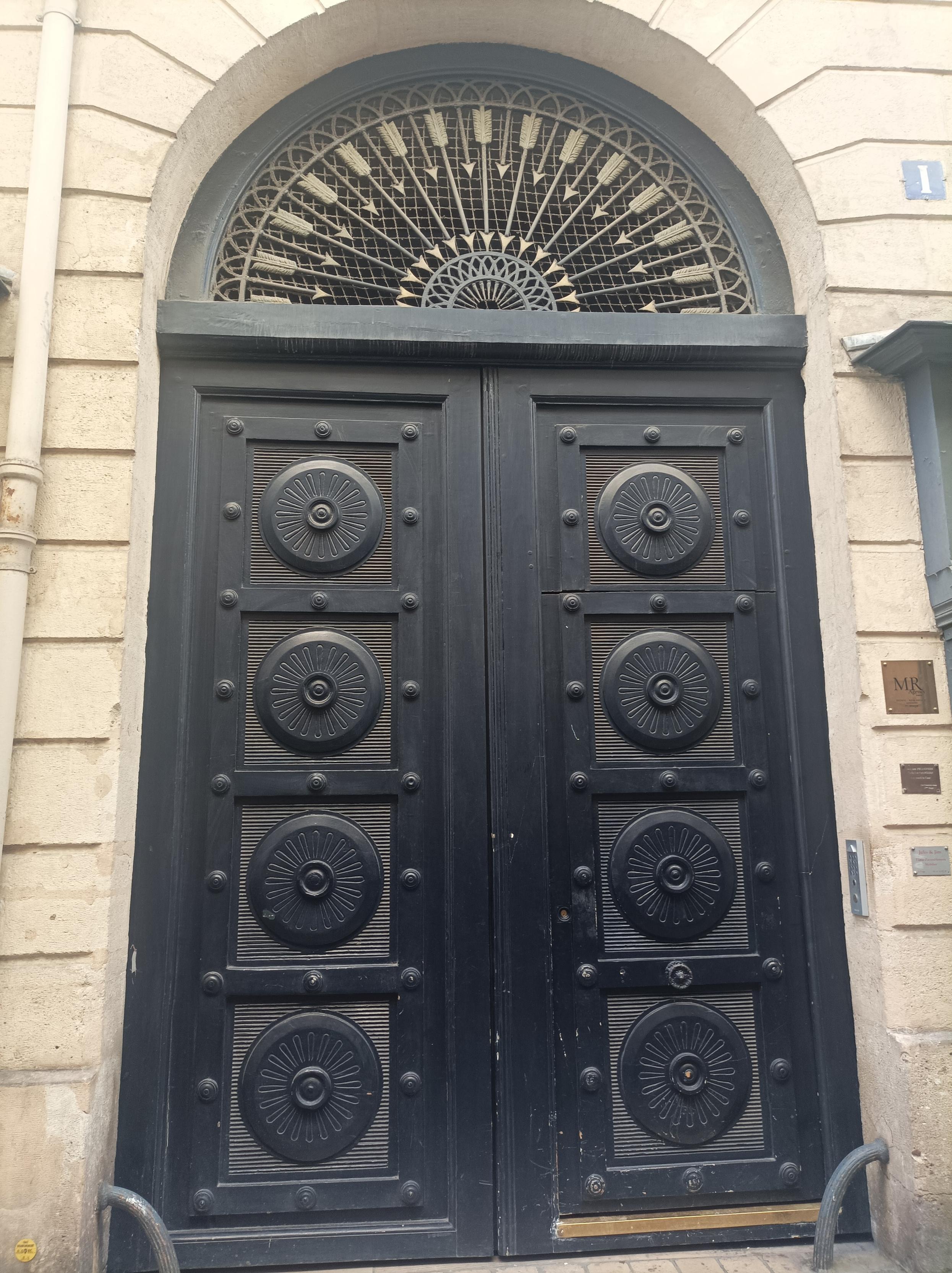 Une porte massive bleue foncée, avec des motifs géométriques, des sphères rappelant des fleurs réparties équitablement sur toute la porte